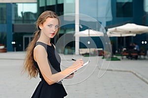 Business woman writing in a folder with documents and looking aw