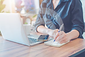 Business woman is writing on a notebook with a pen and using a laptop to work in the office