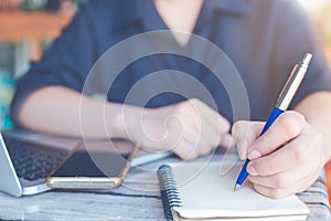 Business woman is writing on a notebook with a pen and using a laptop to work in the office