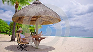 Business woman in yellow hat using laptop computer on the background of a tropical beach with turquoise water. Vacation