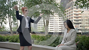 Business women boss is arguing with hers empoyee in the city park and tossing out the folder in anger.