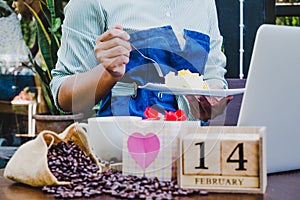 Business women eating cake after using laptop and drinking coffee with 14 February wooden calendar in Valentine day