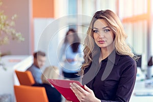 Business woman with folders standing and team mates working in meeting room at office.