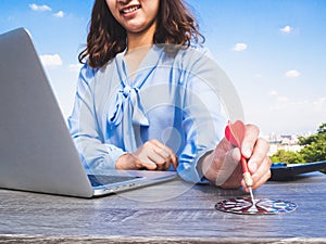 Business women hand point dart to bullseye with calculator and laptop, blue sky and clouds background