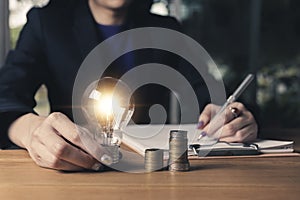 Business women holding light bulb on the desk in office and writing on note book it for financial,accounting,energy,idea concept