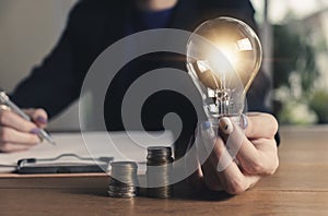 Business women holding light bulb on the desk in office and writing on note book it for financial,accounting,energy,idea concept