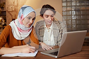 Business. Women Meeting In Cafe. Diversity Ethnic Colleagues Working On Laptop. Girl In Hijab Writing, Brunette Showing Something