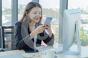 Business women are playing mobile phones Dress well, wear a suit There are many items on the table. And have a desktop computer