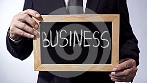 Business written on blackboard, man in suit holding sign, leadership, goals