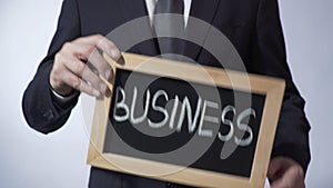 Business written on blackboard, man in suit holding sign, leadership, goals