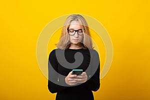 Business young blonde woman, in glasses, dressed in a strict black dress, holds a smartphone, is typing a text message
