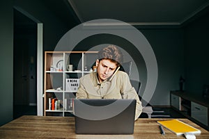 Business young man in a shirt working on a laptop at his desk at home and talking on the phone with a serious face. Busy employee