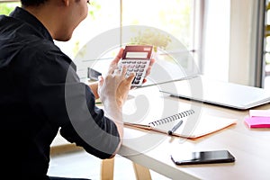 Businessman or accountant Asian young man holding calculator to calculate financial data, cost and budget