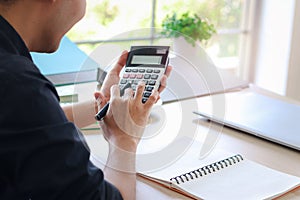 Businessman or accountant Asian young man holding calculator to calculate financial data, cost and budget on desk at home,