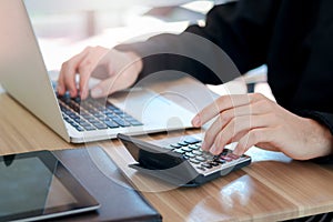 Businessman or accountant hands using calculator and laptop computer to calculate financial data, cost and budget on desk at