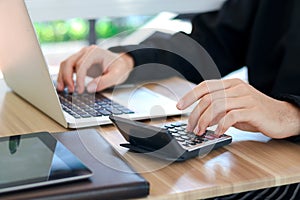 Businessman or accountant hands using calculator and laptop computer to calculate financial data, cost and budget on desk at