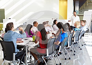 Businessman Addressing Meeting Around Boardroom Table