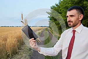 Businessman agronomist farmer in the field holds a wallet with spikelets of wheat