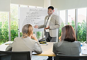 Businessman in airline is standing at board, seriously working and looking at women workers in meeting room. Business group