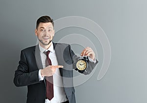 Businessman with alarm clock on gray background. Time management concept