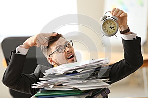 Businessman with alarm clock and stack of documents in office. Time management concept