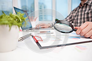 Businessman analyzing business graphs with magnifying glass