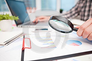 Businessman analyzing business graphs with magnifying glass