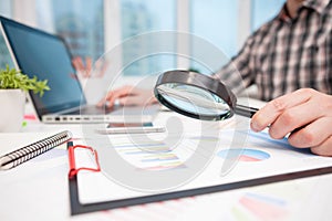 Businessman analyzing business graphs with magnifying glass