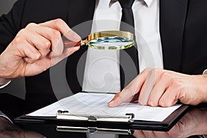 Businessman analyzing document with magnifying glass at desk