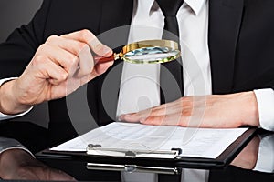 Businessman Analyzing Document With Magnifying Glass At Desk
