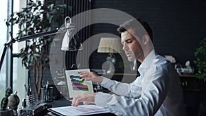 Businessman analyzing financial statistics on documents with graphs on laptop