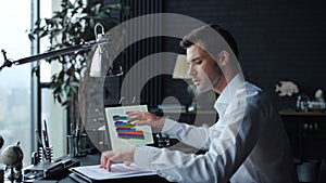 Businessman analyzing financial statistics on documents with graphs on laptop