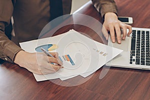 Businessman analyzing graph document with laptop and cell phone in office