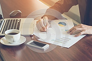 Businessman analyzing graph document with laptop and coffee in office vintage tone