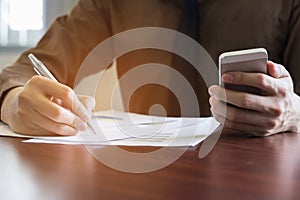 Businessman analyzing graph document with laptop and using cell phone in office