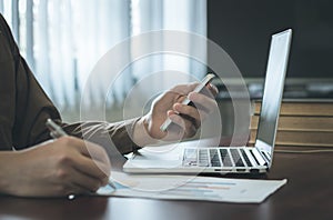 Businessman analyzing graph document with laptop and using cell phone in office