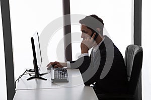 Businessman Answering Mobilephone While Using Computer At Office