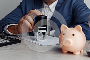 Businessman approves important contract. Piggy bank with stack of coins on desk close-up. Economy, business and