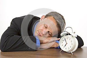 Businessman Asleep On Desk By An Alarm Clock