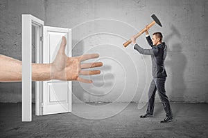 Businessman with axe in hands on the right ready to hit huge human hand reaching out through white doorway on the left.