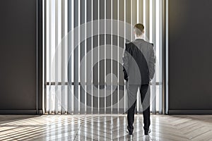 Businessman back view in empty stylish room with parquet floor in front of blinds