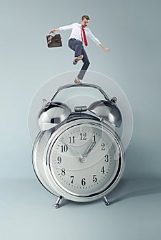 Businessman balancing over alarm clock.