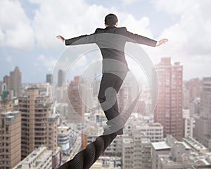 Businessman balancing on a wire with sky clouds cityscape