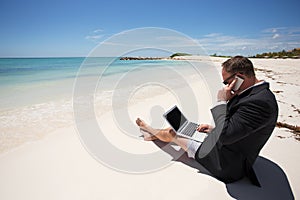 Businessman on the beach working with computer and speaking on phone