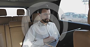 Businessman with a beard working on a laptop while traveling and looking out the window.