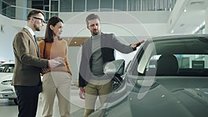 Businessman and beautiful wife choosing car in dealership talking to salesman