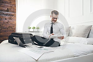 Businessman on bed working with a tablet and laptop from his hotel room