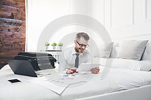 Businessman on bed working with a tablet and laptop from his hotel room