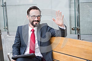 Businessman on bench with tablet welcome colleagues out of office. Professional business people makes meeting in city on bench