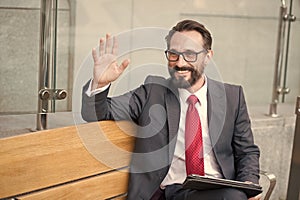 Manager on bench with tablet welcome colleagues out of office. Professional business people meeting outdoor. Happy Bearded man